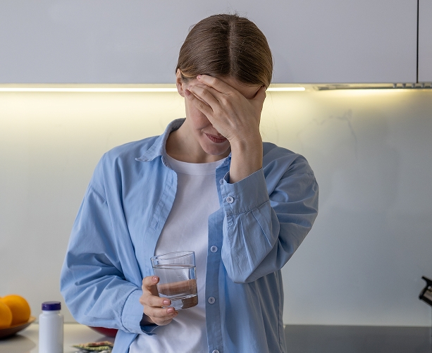 Woman holding a glass of water and covering her face with her hand